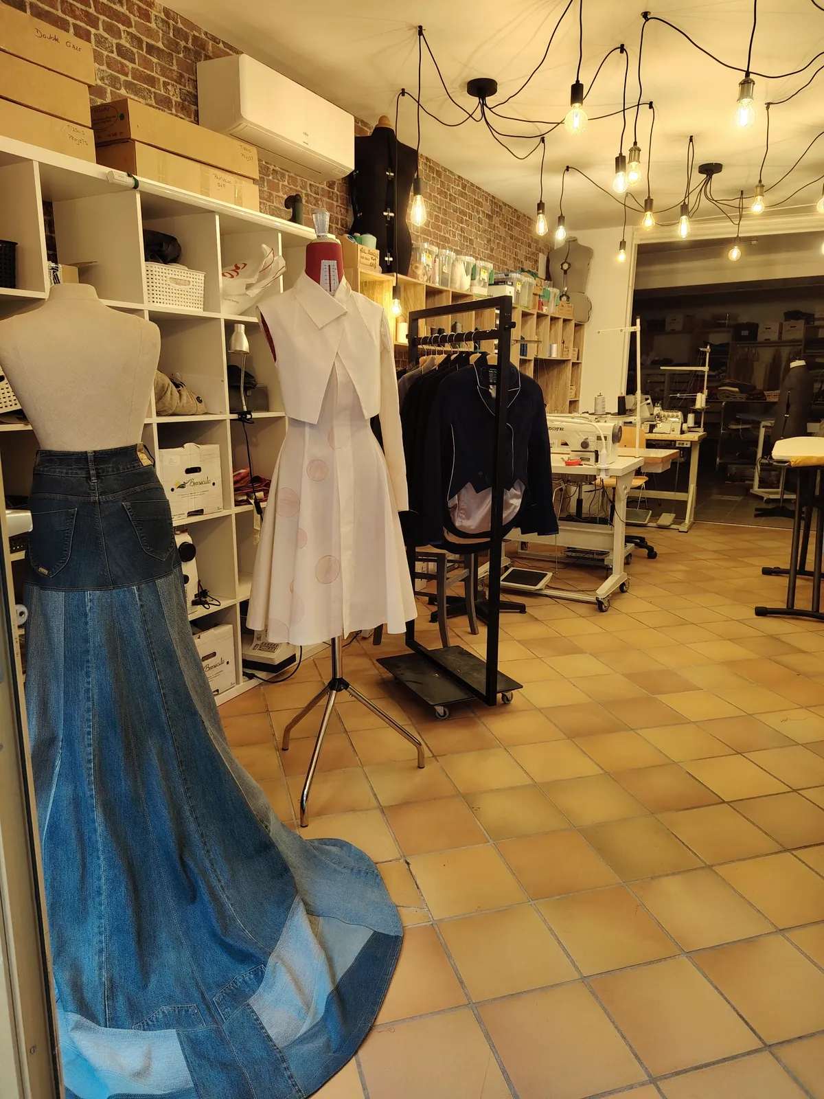 Intérieur de l'atelier : mannequins habillés, étagères de tissus et longue jupe bleue drapée.